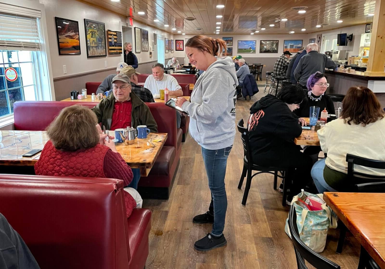 Waitress waiting on a couple sitting in a booth and a variety of diners sitting at tables and booths enjoying their food